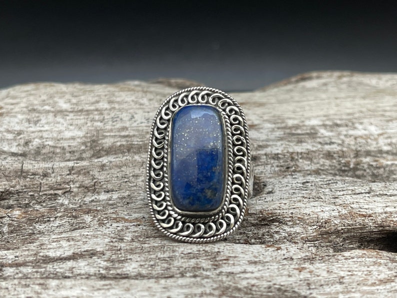 May include: A silver ring with a blue lapis lazuli stone set in a decorative, ornate silver bezel.