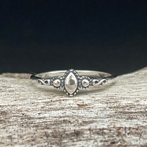 Puede incluir: Un anillo de plata con una piedra central en forma de diamante y detalles intrincados en la banda.