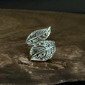 May include: A silver-colored ring with a leaf design. The ring features two openwork leaves that appear to wrap around a finger. The leaves have detailed veining and a textured surface, creating a naturalistic aesthetic.