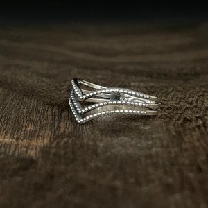 May include: A silver ring with three bands that are connected at the top. The bands are decorated with small beads.