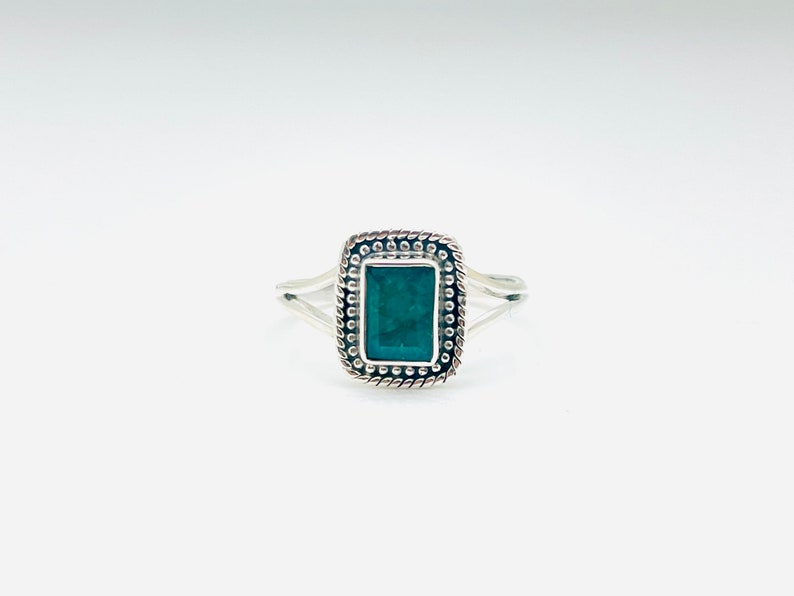 Puede incluir: Un anillo de plata con una piedra rectangular verde oscuro engastada en un marco de plata decorativo.