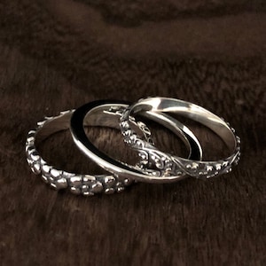 May include: Three silver rings with different textured designs. The rings are stacked on top of each other.