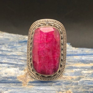 May include: A silver ring with a large, rectangular, faceted ruby gemstone set in a decorative silver bezel.