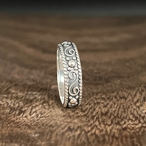 May include: A silver band ring with a decorative design of swirls and beads.