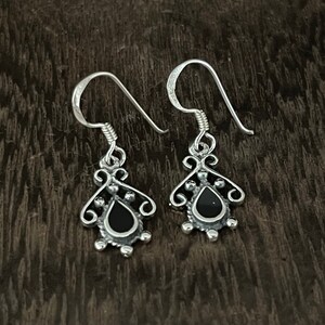 May include: A pair of silver dangle earrings with black teardrop-shaped stones. The earrings have a delicate, ornate design.