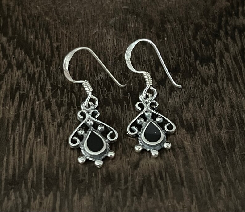 May include: A pair of silver dangle earrings with black teardrop-shaped stones. The earrings have a delicate, ornate design.