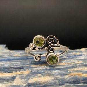 May include: A silver ring with a swirling design and two green gemstones.