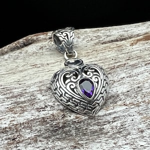 May include: A silver heart-shaped pendant with an intricate filigree design and a purple gemstone in the center.