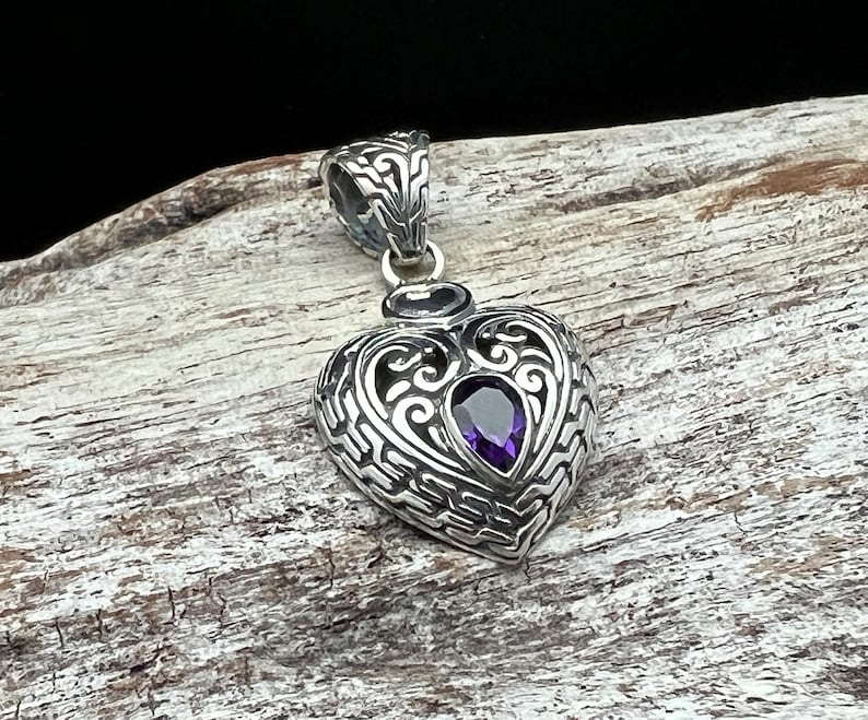 May include: A silver heart-shaped pendant with an intricate filigree design and a purple gemstone in the center.