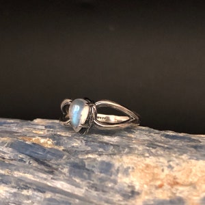 May include: A silver ring featuring a teardrop-shaped moonstone set in the centre. The ring has a delicate, open design.