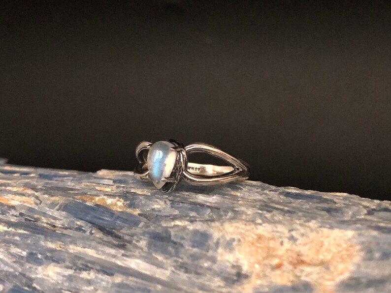 May include: A silver ring featuring a teardrop-shaped moonstone set in the centre. The ring has a delicate, open design.