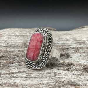 May include: A silver ring with a red and white stone set in a decorative filigree design.