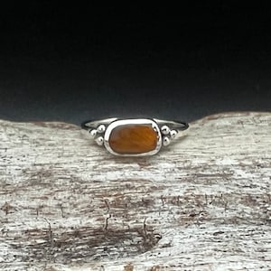 May include: A silver ring with a brown tiger's eye gemstone set in a bezel setting. The ring has small silver beads on either side of the stone.