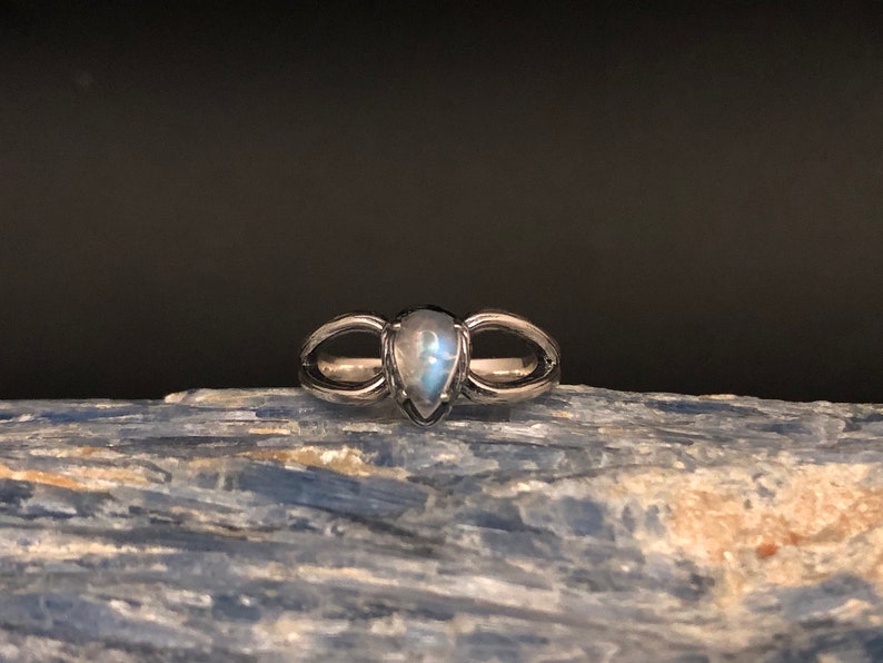 May include: A silver ring featuring a teardrop-shaped moonstone set in the centre. The ring has a delicate design with two curved bands that meet at the stone.