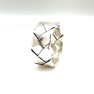 Könnte beinhalten: Ein silberner Ring mit einem geflochtenen Design. Der Ring ist dick und hat eine breite Band.
