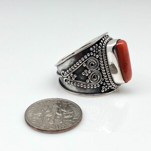 May include: A silver ring with an orange stone set in a decorative band. The band is detailed with a rope design and a swirl pattern.
