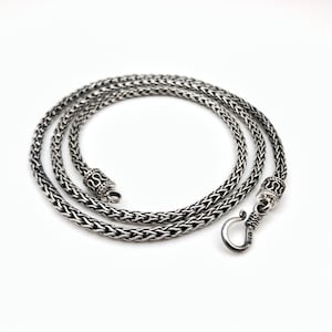 Può includere: Una collana a catena d'argento con chiusura a scatola. La catena è realizzata con un motivo intrecciato.