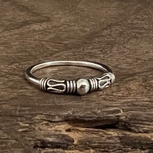 Puede incluir: Un anillo de plata con una banda texturizada y una pequeña cuenta redonda en el centro.