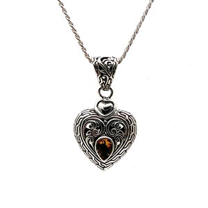 Puede incluir: Un collar con un colgante en forma de coraz&oacute;n de plata con un intrincado dise&ntilde;o de filigrana y una piedra preciosa marr&oacute;n en el centro.