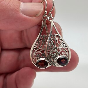 Puede incluir: Pendientes de filigrana de plata con forma de l&aacute;grima y una piedra preciosa de color rojo oscuro en cada pendiente.