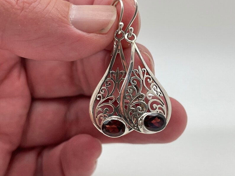 Puede incluir: Pendientes de filigrana de plata con forma de l&aacute;grima y una piedra preciosa de color rojo oscuro en cada pendiente.
