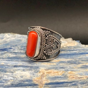 May include: A silver ring with an orange coral stone set in a detailed silver band.