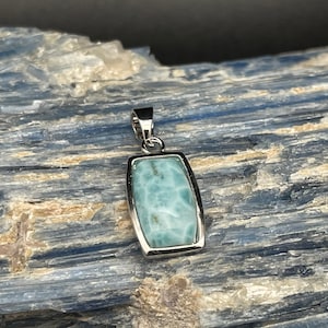May include: A silver pendant with a light blue, rectangular, iridescent gemstone set in a silver frame.
