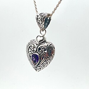 May include: A silver heart-shaped pendant with intricate filigree detailing and a purple amethyst gemstone in the center.