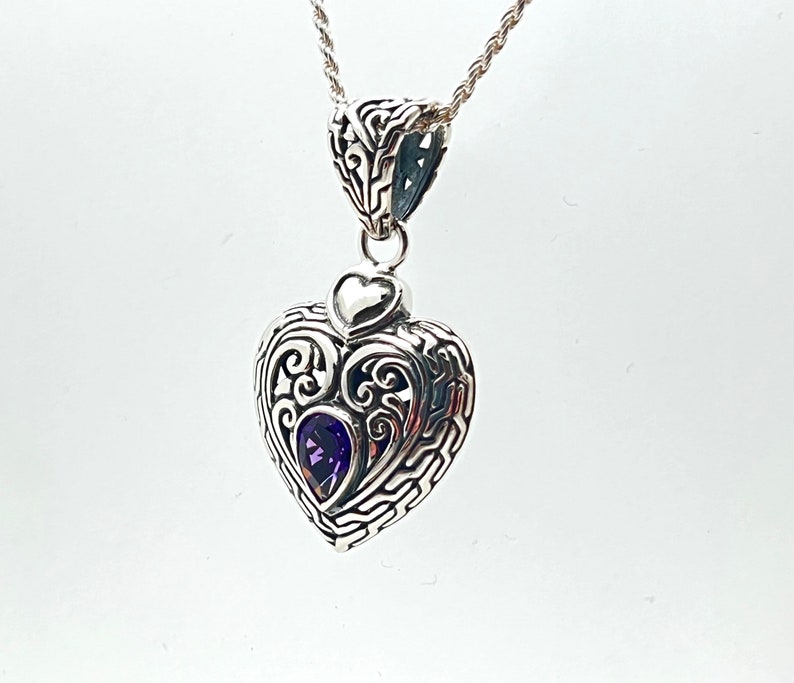 May include: A silver heart-shaped pendant with intricate filigree detailing and a purple amethyst gemstone in the center.