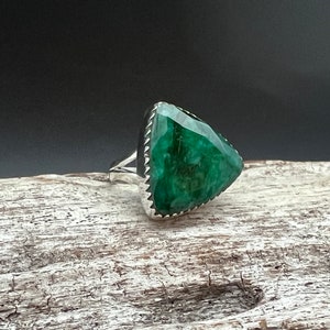May include: A silver ring with a large, triangular, green gemstone. The gemstone has a faceted cut and is set in a silver bezel.