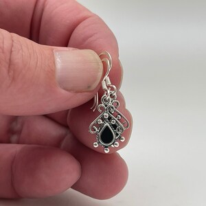 May include: Silver dangle earrings with a black teardrop-shaped stone and intricate filigree design.