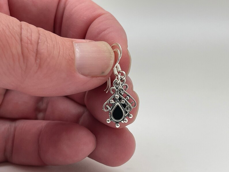 May include: Silver dangle earrings with a black teardrop-shaped stone and intricate filigree design.