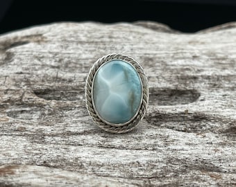 May include: A silver ring featuring a light blue oval gemstone set in a twisted silver band.