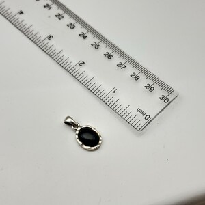 Puede incluir: Un colgante de plata con una piedra negra ovalada, junto a una regla. El colgante mide aproximadamente 2.5 cm de largo. La regla est&aacute; marcada en pulgadas.