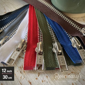 May include: Assortment of 30 cm metal zippers in various colours, including red, white, blue, green, brown, and grey. The zippers have silver metal teeth and sliders. The zippers are laid out on a wooden surface. 12 inch / 30 cm.
