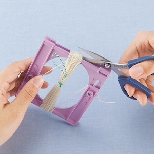 May include: A craft project in progress, featuring a lilac yarn winder and scissors with blue handles. The winder holds beige yarn, and the scissors are cutting the yarn. The background is a light blue.
