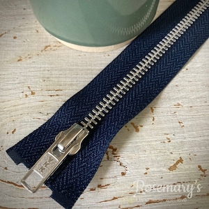 May include: A navy blue zipper with a silver metal slider and teeth. The zipper is lying on a white wooden surface.
