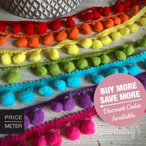 May include: A collection of colorful pom-pom trim ribbons arranged in rows, featuring red, orange, yellow, green, blue, purple, and pink pom-poms attached to a woven fabric tape. A pink circular graphic with white text reads BUY MORE SAVE MORE.