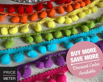 Puede incluir: Una colección de cintas con pompones de colores dispuestas en filas, con pompones rojos, naranjas, amarillos, verdes, azules, morados y rosas unidos a una cinta de tela tejida. Un gráfico circular rosa con texto blanco dice BUY MORE SAVE MORE.