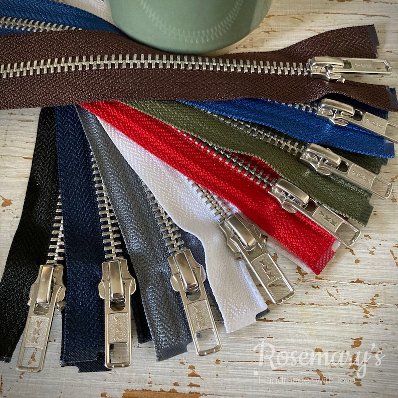 May include: Assortment of metal zippers in various colors, including brown, red, white, green, blue, gray, and navy. The zippers are arranged in a fan shape and have silver teeth.