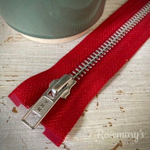 May include: A close-up of a red zipper with a silver metal slider. The zipper is made by YKK and is a popular choice for sewing projects.