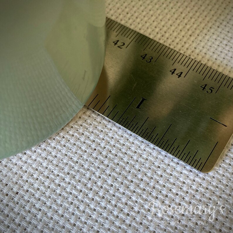 Puede incluir: Primer plano de una regla de metal con marcas del 42 al 45 pulgadas. La regla se coloca sobre una tela blanca con un patr&oacute;n de cuadr&iacute;cula.