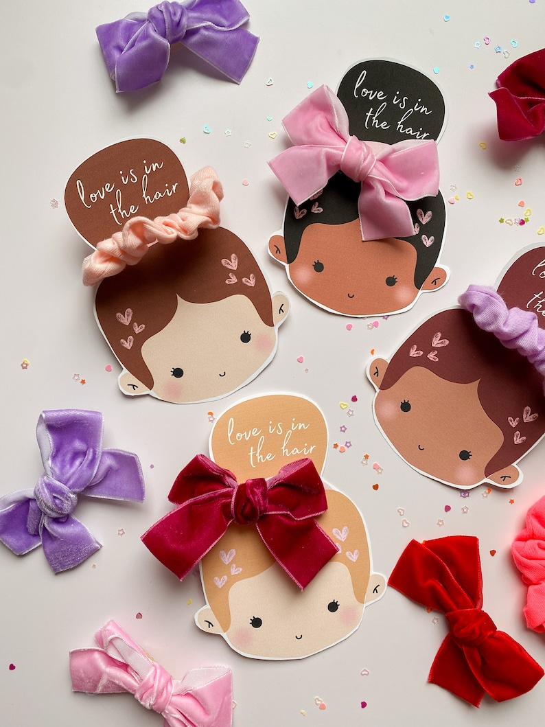 Puede incluir: Cuatro caras ilustradas con diferentes accesorios para el cabello, incluyendo una scrunchie rosa, un lazo de terciopelo rosa, un lazo de terciopelo burdeos y un lazo de terciopelo morado. Cada cara tiene el texto "love is in the hair" escrito encima.