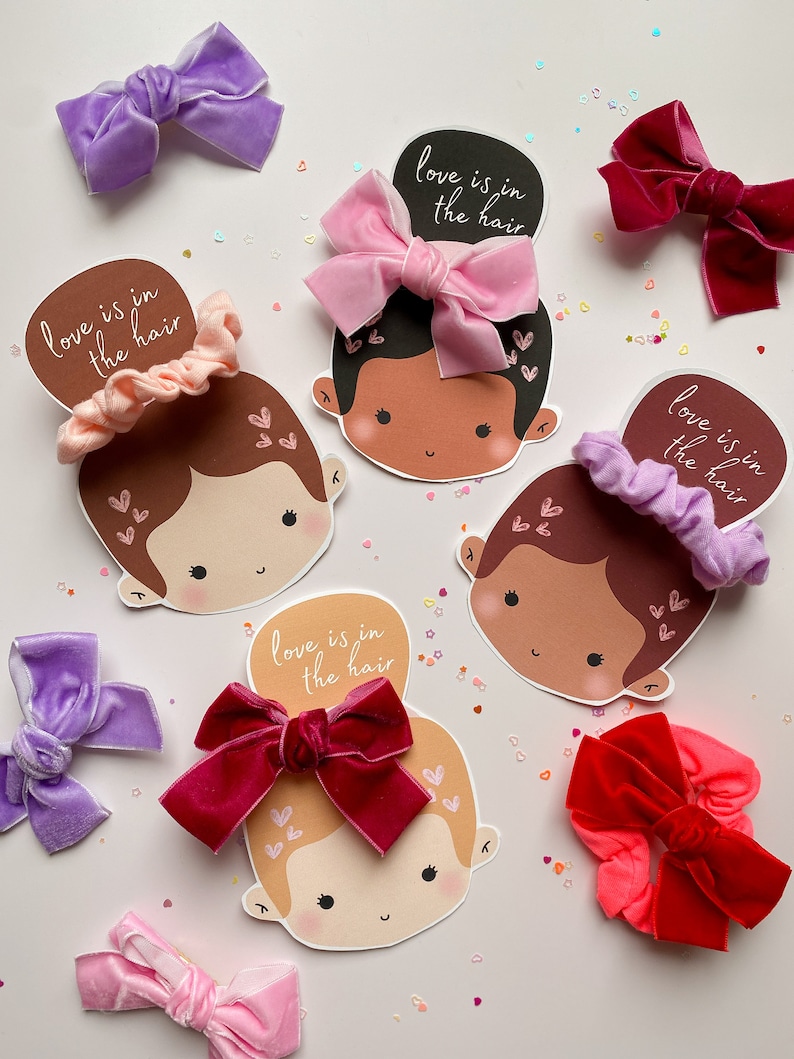 Puede incluir: Cuatro tarjetas ilustradas con caras de dibujos animados y el texto "love is in the hair" en cada tarjeta. Cada tarjeta tiene un lazo de pelo de terciopelo de color diferente en la parte superior. Los lazos de pelo son rosa, morado, rojo y burdeos.