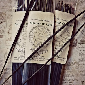 Puede incluir: Tres paquetes de varillas de incienso con etiquetas que dicen "Summer of Love" y "Patchouli/Sandalwood". Las etiquetas presentan un diseño circular con símbolos y texto. El incienso está hecho a mano y mezclado por Symbolry.