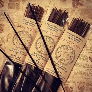 May include: Three packages of brown incense sticks with labels that read "A Peaceful Blend with Frankincense, Myrrh & Rose" and "SANCTUARY". The labels also feature a circular design with symbols and the text "Custom Blended, Hand Dipped Incense by Symbolry".