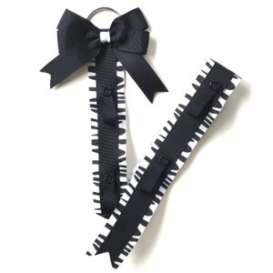 Può includere: Due porta fiocchi per capelli bianchi e neri. Uno ha un grande fiocco nero con un accento bianco e un anello argentato. I porta fiocchi hanno un motivo zebrato e nastro nero con bottoni a pressione.