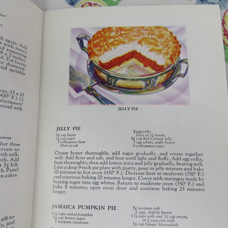 May include: An illustration of a Jelly Pie, a dessert with a red filling and a golden-brown crust, served in a silver dish. The image is from a vintage cookbook, with text describing the recipe.