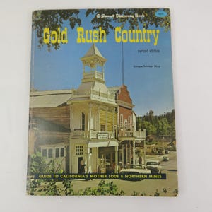 Puede incluir: Un libro de tapa blanda titulado Gold Rush Country, un Sunset Discovery Book, que presenta una fotografía de un edificio histórico con una torre blanca, un letrero de museo y coches antiguos en una calle. La portada incluye el texto Guide to California's Mother Lode & Northern Mines y Unique Foldout Map.