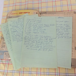 May include: A collection of handwritten recipes on light green paper, featuring canning instructions for vegetables. The recipes are on a yellow and white checkered tablecloth, with a vintage canning guide visible in the background.